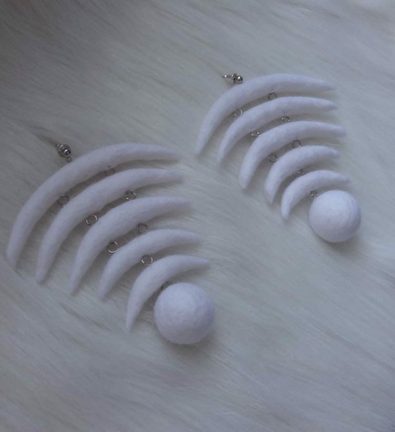 May include: A pair of white felt earrings with a crescent moon shape and a round ball at the bottom.