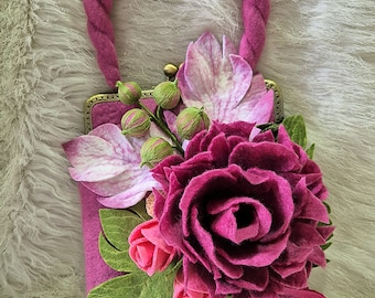May include: A pink felt purse with a floral design. The purse has a clasp closure and a pink felt handle. The flowers are made of felt and include a large pink rose, smaller pink roses, and green leaves.