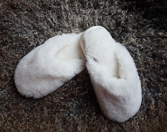 May include: A pair of white fluffy slippers with a soft, fuzzy texture. The slippers are laid out on a brown, curly, furry surface.