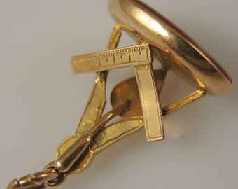 May include: A gold-toned seal with a red stone and a decorative, engraved design. The seal is attached to a chain.