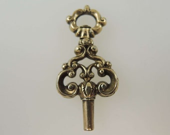 May include: A gold-toned ornate key with a decorative, scrolled design. The key has a loop at the top and a long, thin shaft.
