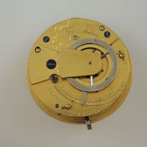 May include: A gold pocket watch with a round face and a silver dial. The watch has a lever on the side for setting the time. The watch face has the inscription "J. Parkinson & Frodsham London" and a scale marked "Slow" and "Fast".