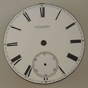 May include: White clock face with black Roman numeral hour markers and black minute markers. The clock face has a smaller white clock face inside with black minute markers. The clock face has the text "ROBT. HOSKRELL LIVERPOOL" printed on it.
