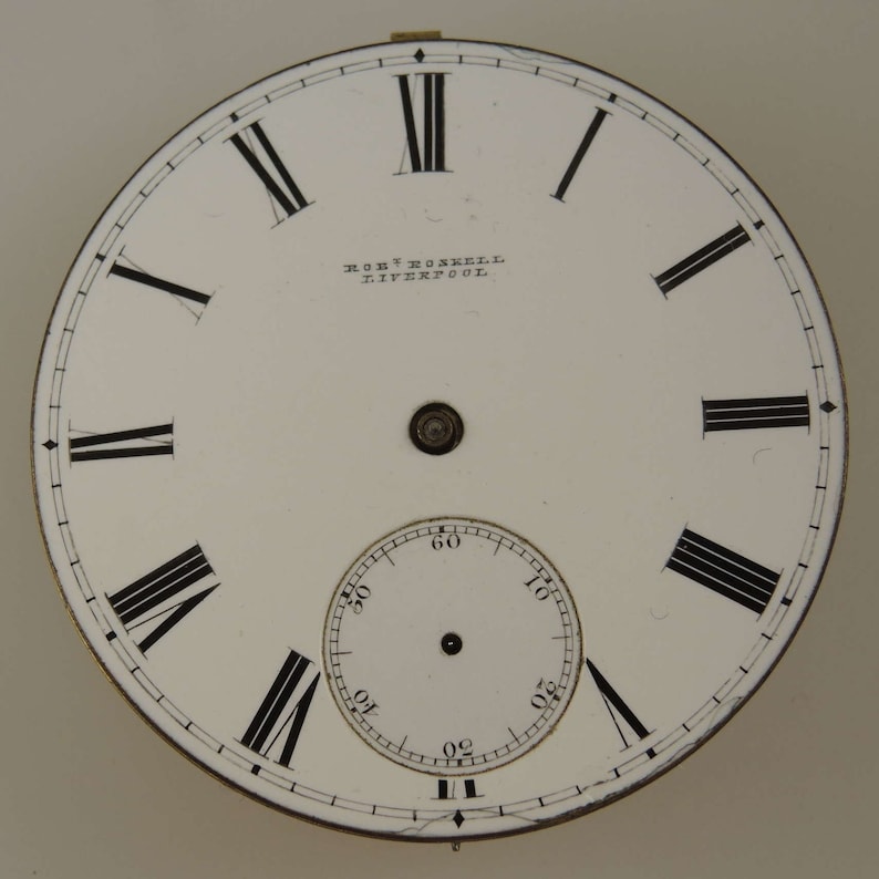 May include: White clock face with black Roman numeral hour markers and black minute markers. The clock face has a smaller white clock face inside with black minute markers. The clock face has the text "ROBT. HOSKRELL LIVERPOOL" printed on it.