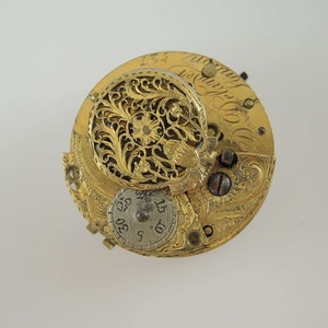 K&ouml;nnte beinhalten: Eine goldfarbene Taschenuhr mit aufwendigen Gravuren und einem filigranen, durchbrochenen Design. Das Zifferblatt der Uhr ist sichtbar und zeigt r&ouml;mische Ziffern und ein kleines, kreisf&ouml;rmiges Zifferblatt.