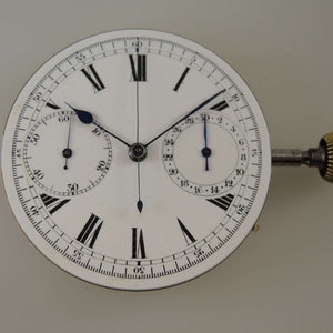 May include: A white chronograph watch face with black Roman numeral hour markers and black minute markers. The watch has two sub-dials, one for seconds and one for minutes. The watch has a gold winding stem.