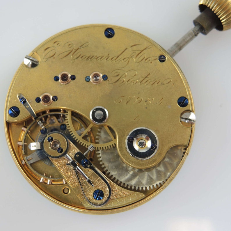 Puede incluir: Primer plano de un movimiento de reloj de bolsillo de color dorado con la inscripci&oacute;n "E. Howard & Co. Boston" y el n&uacute;mero "57981".