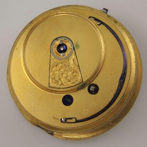 May include: A detailed view of a gold-coloured pocket watch mechanism. The interior showcases intricate engravings and small screws. A curved, dark blue element arcs across the top. The watch's design is circular.