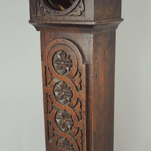 Peut inclure: Une horloge ancienne en bois brun foncé avec des sculptures florales complexes. L'horloge présente une ouverture ronde en haut et des sculptures décoratives sur le panneau avant. La base présente également des motifs floraux sculptés.