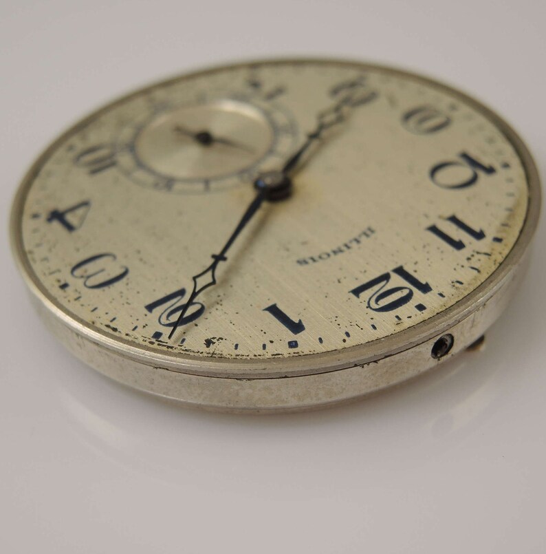 Op de afbeelding: Een zilveren zakhorloge met zwarte wijzers en Romeinse cijfers. Het horloge heeft een licht verweerd gezicht en een klein sub-horloge. Het horloge is gemarkeerd met "Blomquist" op het gezicht.