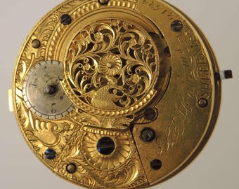 May include: Close-up of a gold pocket watch movement. The intricate design features ornate floral patterns, a small subdial, and engraved text. The watch mechanism is a complex arrangement of gears and screws, showcasing fine craftsmanship.