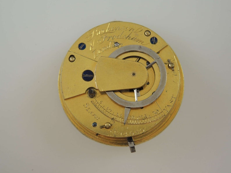 May include: A gold pocket watch with a round face and a silver dial. The watch has a lever on the side for setting the time. The watch face has the inscription "J. Parkinson & Frodsham London" and a scale marked "Slow" and "Fast".