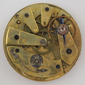 May include: Close-up of a gold-toned pocket watch movement with intricate gears and levers. The watch face is visible in the background.