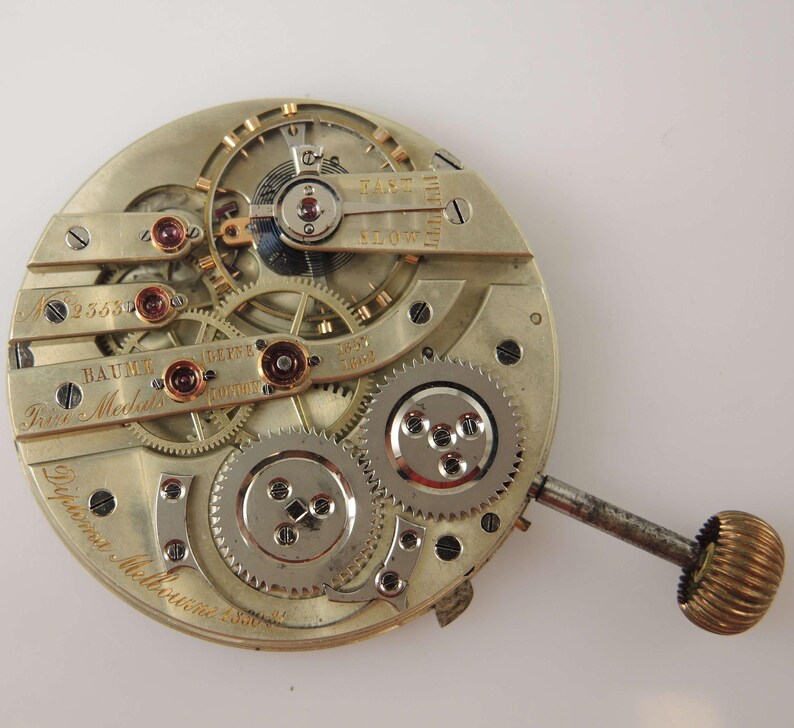 Puede incluir: Un movimiento de reloj de bolsillo de plata con engranajes intrincados y un v&aacute;stago de cuerda. El reloj est&aacute; etiquetado como "Baume & Co. Gen&egrave;ve" y "Prix M&eacute;daille d'Or" con el n&uacute;mero de serie "25632".
