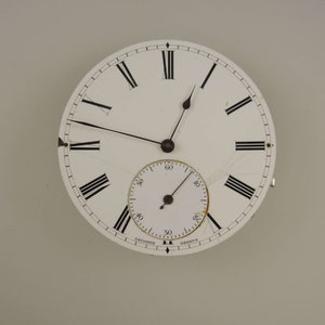 Op de afbeelding: Een wit zakhorloge-horloge met zwarte Romeinse cijfers voor de uren en zwarte wijzers. De wijzerplaat van het horloge heeft een kleinere, witte secondenwijzerplaat met zwarte markeringen.