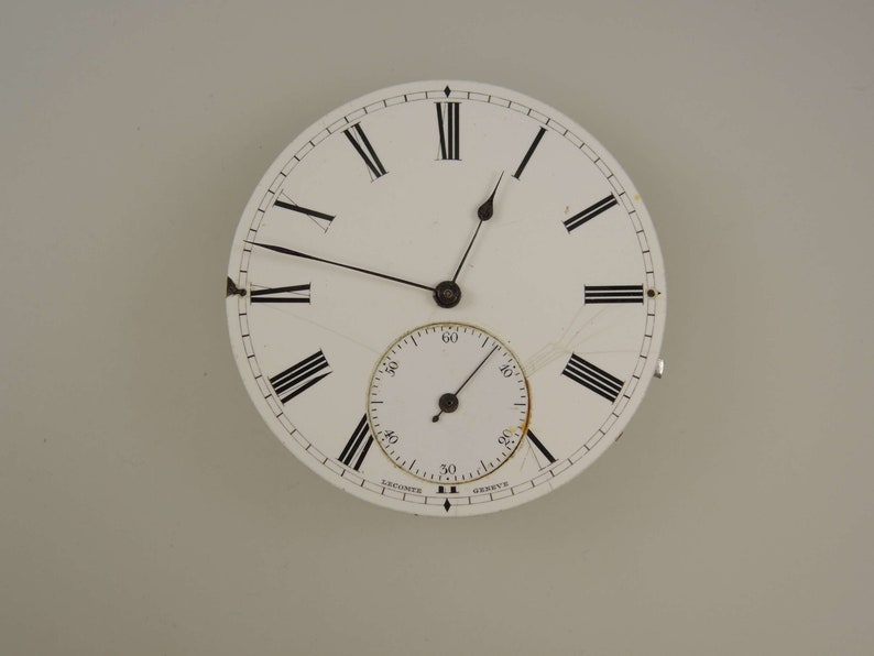 Op de afbeelding: Een wit zakhorloge-horloge met zwarte Romeinse cijfers voor de uren en zwarte wijzers. De wijzerplaat van het horloge heeft een kleinere, witte secondenwijzerplaat met zwarte markeringen.