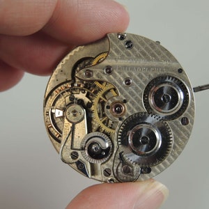 May include: Close-up of a silver pocket watch movement with intricate gears and a patterned back plate. The watch is labeled "J.S. DIME & SON PHILADELPHIA".