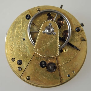 Puede incluir: Primer plano de un movimiento de reloj de bolsillo de oro con la inscripci&oacute;n "The Sentry 14 Carat 1859" y "Patent Henry" visible. El reloj tiene una corona de cuerda plateada y una aguja negra.