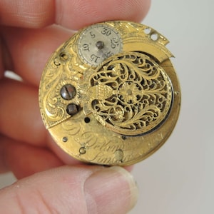 K&ouml;nnte beinhalten: Eine goldene Taschenuhr mit aufwendigen floralen Gravuren auf der R&uuml;ckseite. Das Zifferblatt der Uhr ist sichtbar und hat r&ouml;mische Ziffern f&uuml;r die Stunden.