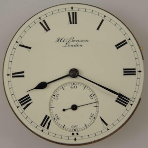 May include: A white pocket watch face with black Roman numeral hour markers and black hands. The watch face has a smaller, concentric circle with black markings for seconds. The watch face is inscribed with "J.W. Benson London".