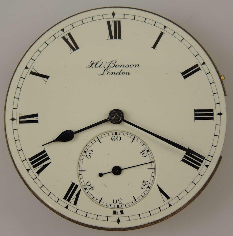 May include: A white pocket watch face with black Roman numeral hour markers and black hands. The watch face has a smaller, concentric circle with black markings for seconds. The watch face is inscribed with "J.W. Benson London".