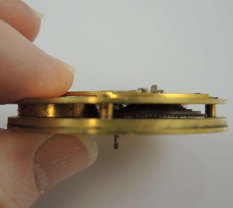 May include: Close-up side view of a gold-colored watch movement with visible gears and a brass frame.