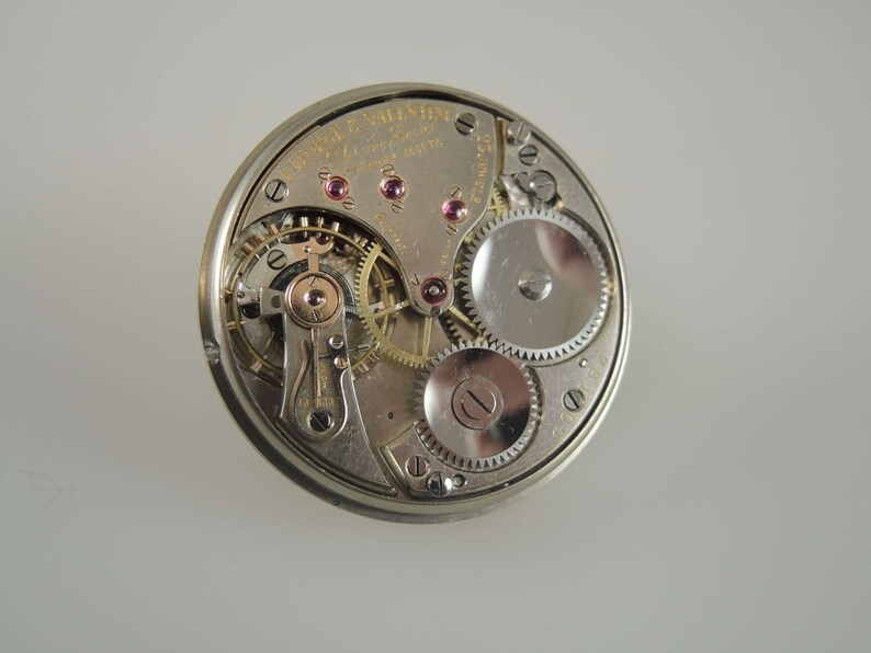 K&ouml;nnte beinhalten: Nahaufnahme des Innenlebens einer silbernen Taschenuhr. Das Zifferblatt der Uhr ist mit dem Text "Waltham  Valentine  17 Jewels  10 Size  Adjusted  to Temperature  and  Five Positions" sichtbar.