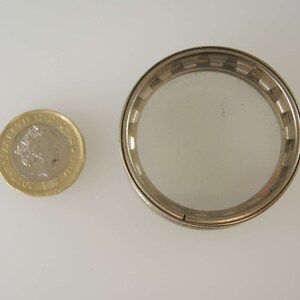 Puede incluir: Un recipiente redondo de metal plateado con una tapa de vidrio transparente. El recipiente es aproximadamente del tama&ntilde;o de una moneda de un euro.