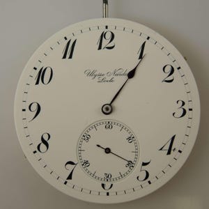 May include: A white pocket watch face with black Roman numeral hour markers and black hands. The watch face also features a smaller, white sub-dial with black markings. The watch face is inscribed with "Ulysse Nardin Locle".
