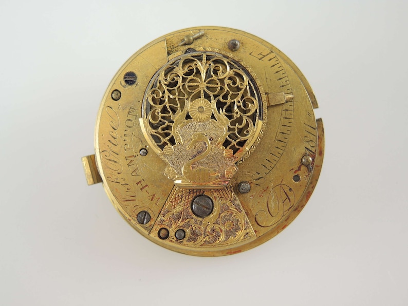 K&ouml;nnte beinhalten: Nahaufnahme eines antiken Uhrwerks aus Gold mit aufwendigen Filigran- und Gravurdetails. Der Uhrenmechanismus zeigt ein dekoratives Schwanen-Emblem und die Inschrift "H-A Hampton". Das Zifferblatt hat ein kreisf&ouml;rmiges Design mit sichtbaren Zahnr&auml;dern und Schrauben.