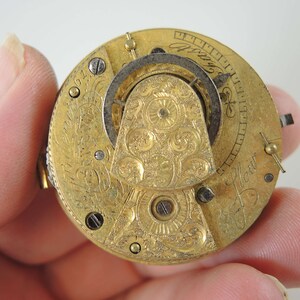 K&ouml;nnte beinhalten: Nahaufnahme eines goldenen Taschenuhrwerks mit aufwendigen floralen Gravuren. Das Zifferblatt der Uhr ist mit r&ouml;mischen Ziffern und der Inschrift "J. How." sichtbar.