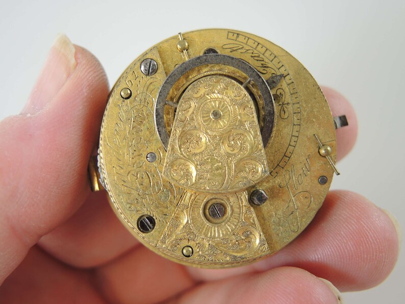 K&ouml;nnte beinhalten: Nahaufnahme eines goldenen Taschenuhrwerks mit aufwendigen floralen Gravuren. Das Zifferblatt der Uhr ist mit r&ouml;mischen Ziffern und der Inschrift "J. How." sichtbar.