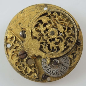 May include: A gold-toned pocket watch with an intricate, open-faced design. The watch face features a circular, openwork pattern with floral motifs and a smaller, circular dial with numbers.