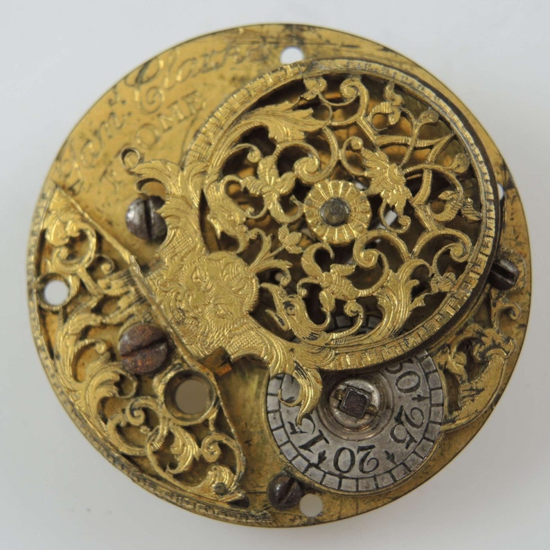 May include: A gold-toned pocket watch with an intricate, open-faced design. The watch face features a circular, openwork pattern with floral motifs and a smaller, circular dial with numbers.