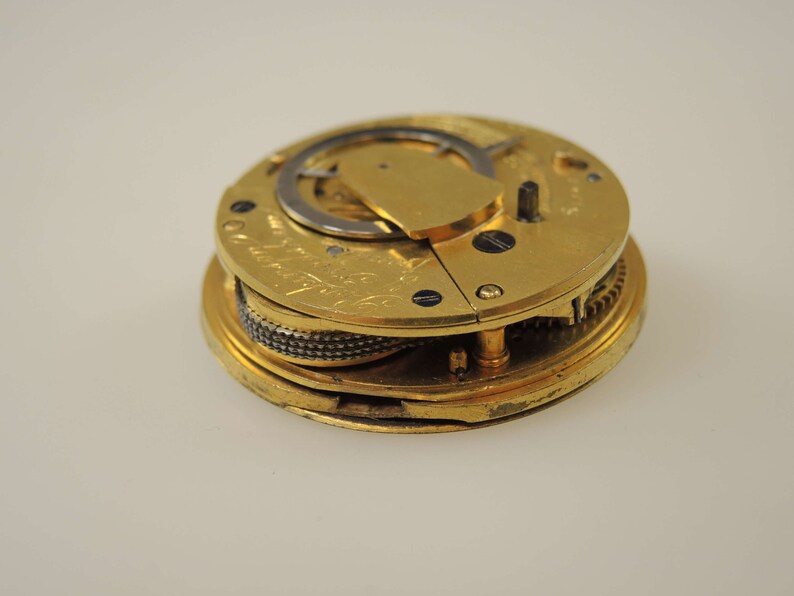 May include: A gold-colored pocket watch movement with intricate gears and a winding mechanism. The watch is open and the inner workings are visible.