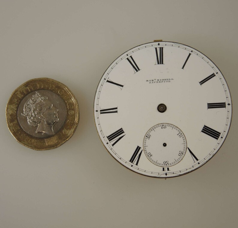 May include: A white pocket watch face with black Roman numeral hour markers and black minute markers. The watch face has a small, white sub-dial with black markings. The watch face is inscribed with "MORT. MASKELL. LIVERPOOL."