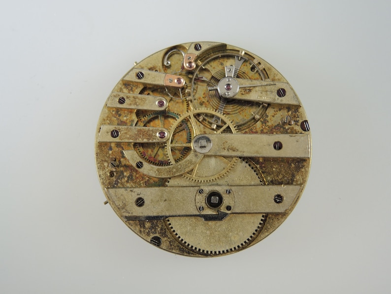 May include: Detailed view of a vintage watch movement, revealing complex gears, levers, and a balance wheel. The mechanism is predominantly gold-coloured with copper and red highlights. The watch parts are arranged on a circular base.