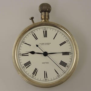 K&ouml;nnte beinhalten: Eine silberfarbene Taschenuhr mit wei&szlig;em Zifferblatt und schwarzen r&ouml;mischen Ziffern. Die Uhr tr&auml;gt den Text "ULYSSE NARDIN LOCLE SUISSE" und die Nummer "123796". Sie hat eine Krone und einen kleinen Knopf. Durchmesser ca. 5 cm.