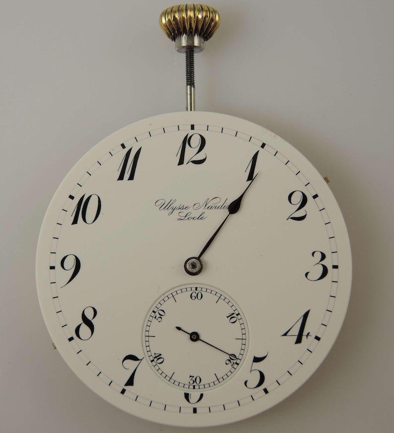 May include: A white pocket watch with black Roman numeral hour markers and black hands. The watch face also includes a smaller subdial with black markings. The watch is labeled "Ulysse Nardin Locle".