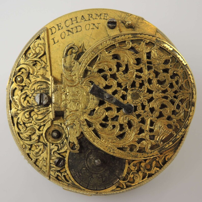 May include: A gold pocket watch with intricate floral engravings and the inscription "De Charme London" on the face.