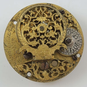 May include: A gold-toned pocket watch with intricate openwork design and the inscription "I am Guillaume Fromont" on the face.