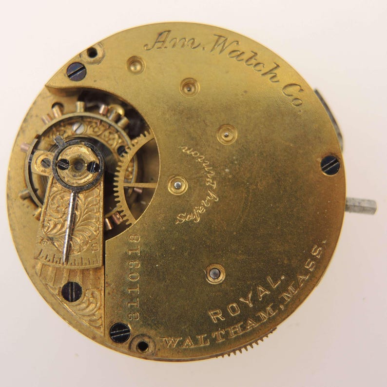 May include: Close-up of a vintage watch movement with intricate gears and engraved details. The gold-toned metal plate features the text "Am. Watch Co." and "ROYAL. WALTHAM, MASS.". The serial number "8110318" is also visible.
