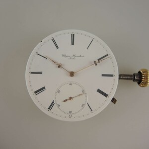 Op de afbeelding: Een wit zakhorloge-wijzerplaat met zwarte Romeinse cijfers voor de uren en zwarte markeringen voor de minuten. De wijzerplaat heeft een goudkleurige opwindstift en wijzers. Op de wijzerplaat staat de tekst "Ulysse Nardin" en "Le Locle".