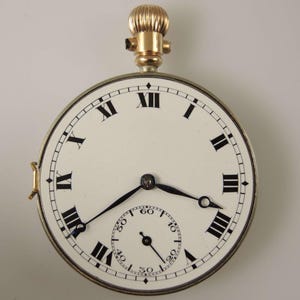 Puede incluir: Un reloj de bolsillo vintage con esfera blanca, n&uacute;meros romanos negros y manecillas negras. El reloj tiene un peque&ntilde;o dial de segundos y una corona y detalles dorados. La caja del reloj es de color plateado.