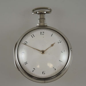 Könnte beinhalten: Eine silberne Taschenuhr mit weißem Zifferblatt und schwarzen römischen Ziffern für die Stunden. Die Uhr hat einen goldfarbenen Stunden- und Minutenzeiger.
