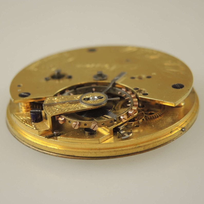 May include: Close-up of a gold pocket watch movement with intricate gears and a winding mechanism.