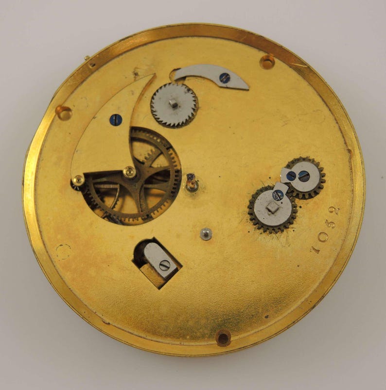 May include: Close-up of the inner workings of a gold-toned pocket watch. The watch face is missing, but the intricate gears and levers are visible. The number "10592" is printed on the watch case.