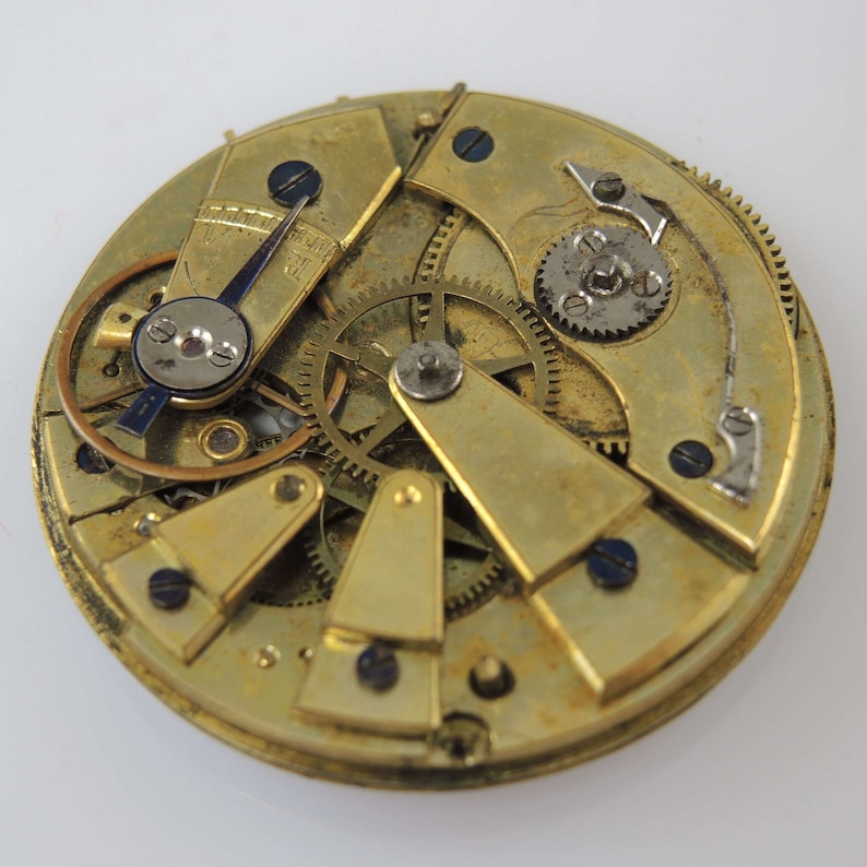 May include: Close-up of a gold-toned pocket watch movement with intricate gears and levers. The watch face is not visible.