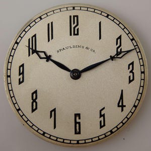 May include: A white watch face with black Roman numeral hour markers and black hands. The watch face has a black border with a repeating pattern of small squares. The text "SPAULDING & CO." is printed in black at the top of the watch face.