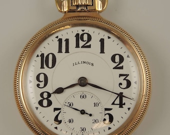 May include: A gold pocket watch with a white face and black Roman numeral hour markers. The watch has a smaller sub-dial for seconds and the text "ILLINOIS" printed on the face.
